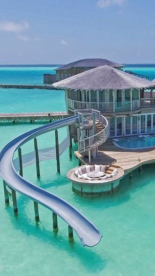 An overwater villa and its water slide above a turquoise lagoon