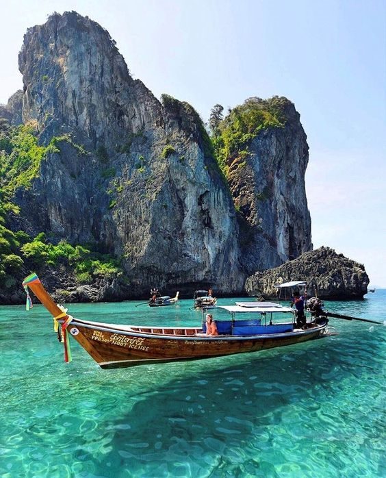 A longtail boat on turquoise water below limestone cliffs