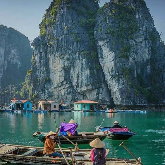 Boats moored below limestone islands in a green bay