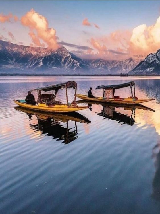 Boats on a still lake at sunset with mountains behind
