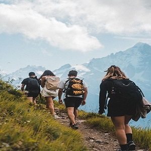 Walkers with backpacks on a green ridge below snow peaks