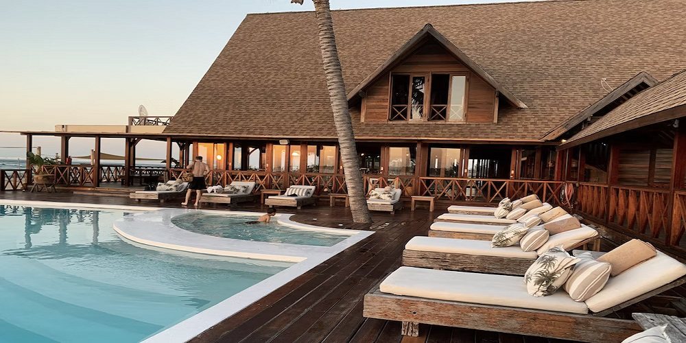 A resort pool deck with loungers in front of a thatched building